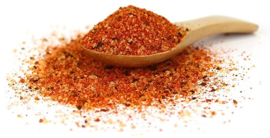Nahaufnahme einer roten Gewürzmischung auf einem Holzlöffel, verteilt auf weißem Hintergrund