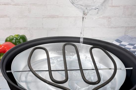 Nahaufnahme eines Dampfgarers, der mit Wasser befüllt wird, sichtbares Heizelement.