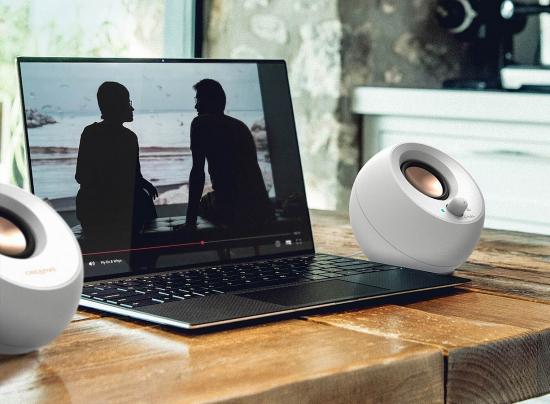 Ein Laptop spielt ein Video ab, flankiert von zwei weißen Lautsprechern auf einem Holztisch.