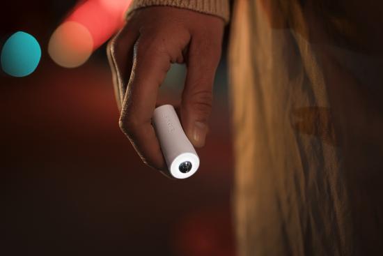 Tragbare LED-Taschenlampe in Hand gehalten Eine Person hält eine kleine, tragbare LED-Taschenlampe in der Hand, abgebildet bei Nacht mit unscharfem, buntem Hintergrundlicht.