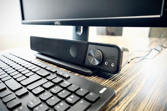 Kompakte Soundbar für den Schreibtisch mit Lautstärkeregler Soundbar mit Lautstärkeregler neben einem Computerbildschirm und Tastatur auf einem Schreibtisch