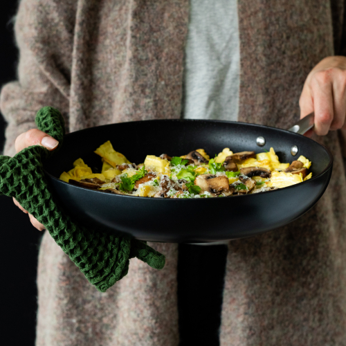 Person hält Bratpfanne mit zubereitetem Omelett, Pilzen und Kräutern in der Hand