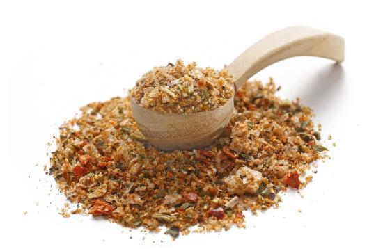 Nahaufnahme eines Holzlöffels, der mit einer bunten Gewürzmischung gefüllt ist, auf weißem Hintergrund