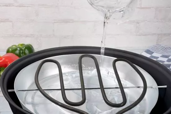 Nahaufnahme eines Dampfgarers, der mit Wasser befüllt wird, sichtbares Heizelement.