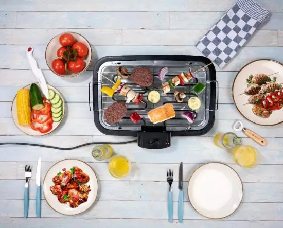 Elektrogrill mit Gemüse, Fleisch und Fisch mit Beilagen wie Salat, Tomaten und Getränken